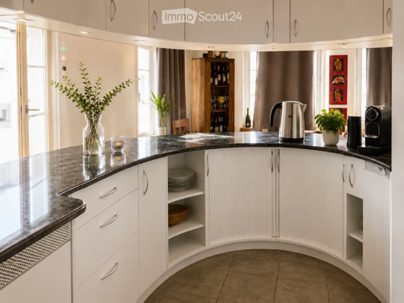 Modern kitchen with white cabinets, black granite countertop, and various appliances including a teapot, coffee maker, and decorative items like vases and candles.