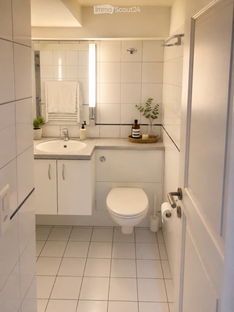 Modern bathroom with white tiles, a sink, a toilet, a mirror, and a small plant on the counter.