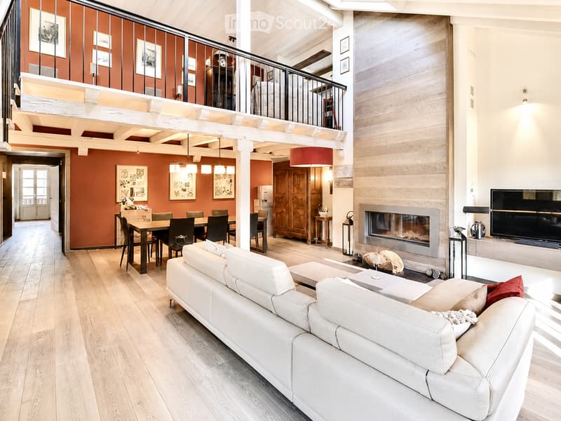 Open-plan living and dining area with a white sectional sofa, coffee table, fireplace, TV, dining table with chairs, and a wooden cabinet.