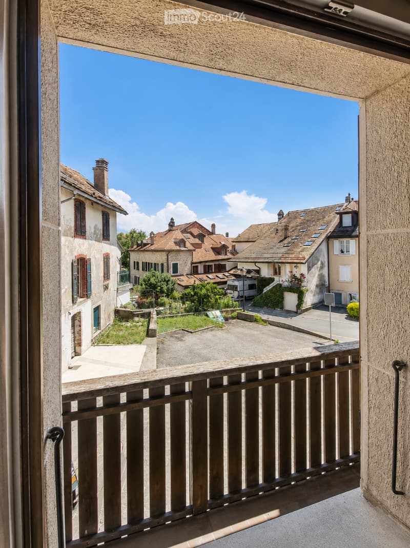 Balcony overlooking a residential area with traditional houses, a clear blue sky, and a small garden below.