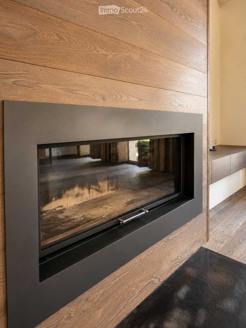 Modern fireplace with sleek black frame and glass front, set against a wooden wall with a polished wooden floor and black rug.