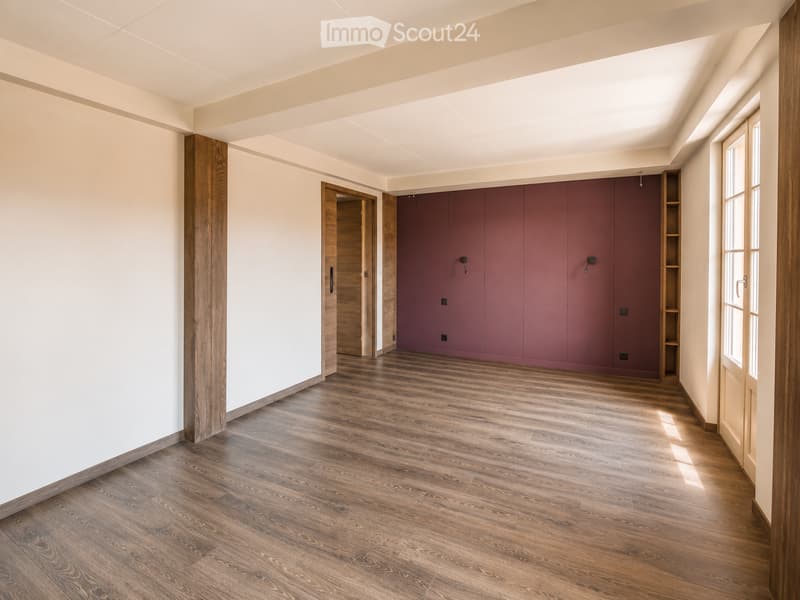 Empty room with wooden flooring, white walls, and a large window allowing natural light. Features a built-in closet with purple doors and a small open shelving unit.