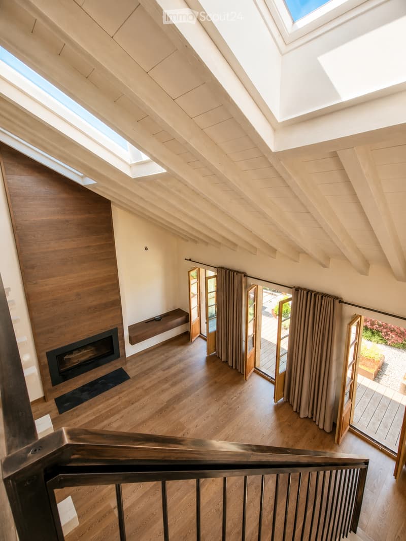 Loft-style living space with wooden floors, exposed wooden beams, skylights, and a fireplace. Features large sliding glass doors leading to an outdoor deck.