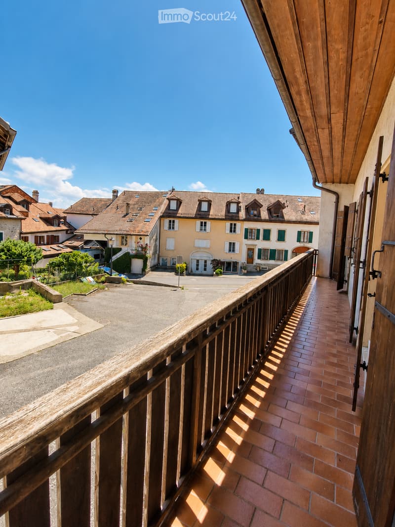 Balcony overlooking a picturesque village with traditional houses, tiled roofs, and a clear blue sky.