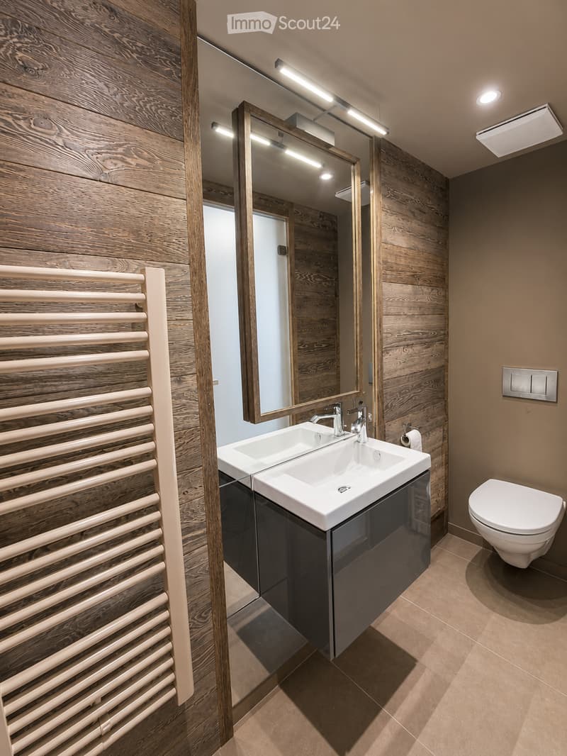 Modern bathroom with wooden walls, a double sink, a large mirror, a radiator, and a toilet.