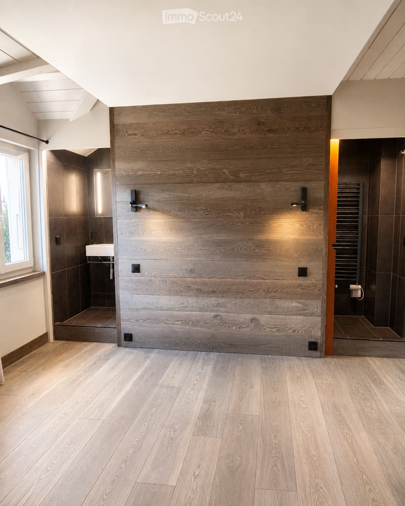 Modern bathroom with wooden plank wall, light wooden flooring, a sink, a mirror, and a radiator. The space is well-lit with natural light from a window on the left side.