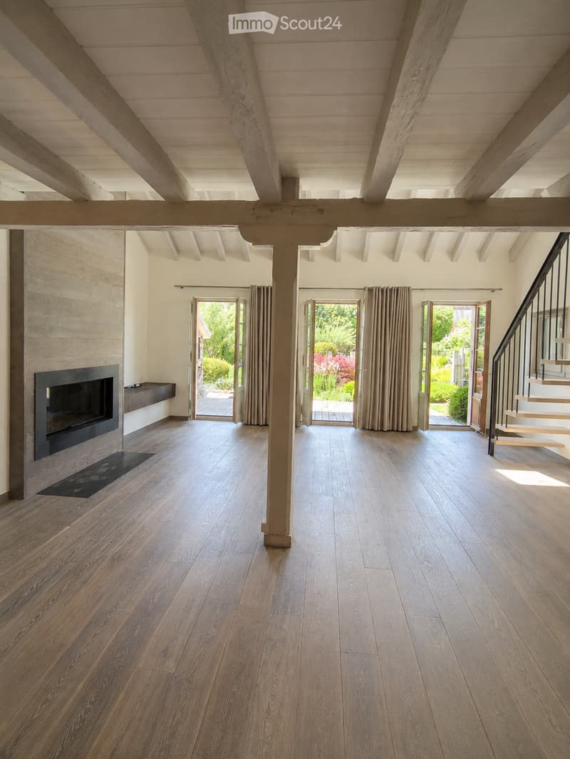 Spacious living room with exposed wooden beams, hardwood flooring, fireplace, and large sliding glass doors leading to outdoor area.