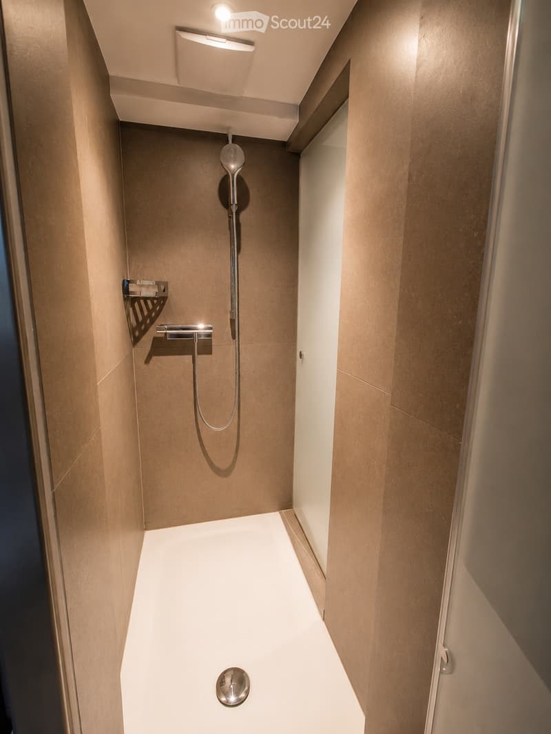 Modern bathroom with a sleek, white bathtub, a handheld showerhead, a chrome faucet, and a small shelf for toiletries.