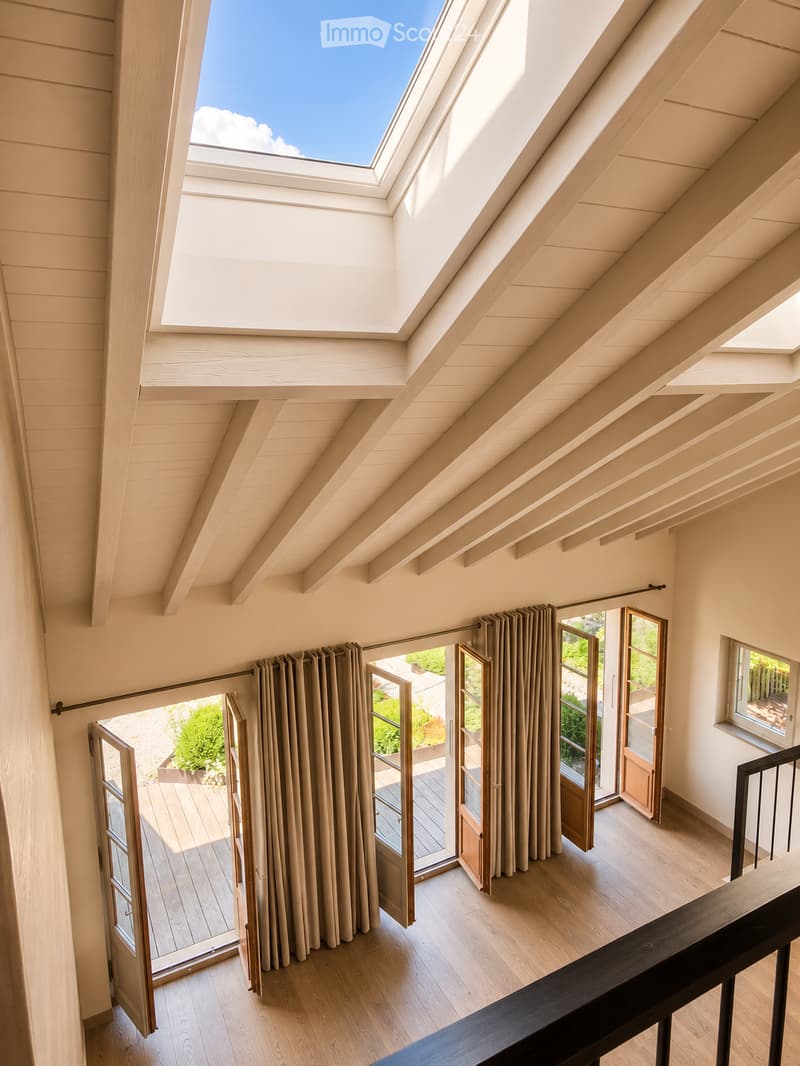 Bright, airy hallway with wooden flooring, large skylight, and open sliding doors leading to a wooden deck and garden area.