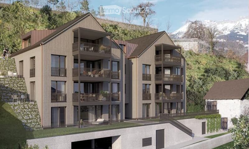 Modern multi-story residential building with balconies, large windows, and a raised ground floor. The building features a contemporary design with wooden and concrete elements, situated in a scenic, elevated location with a view of mountains in the backgr