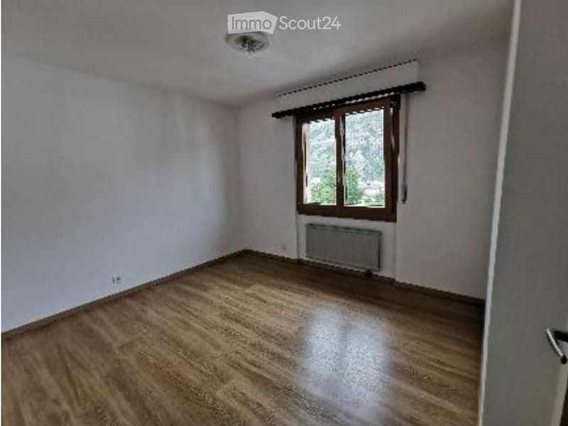 Empty room with wooden flooring, white walls, a single window with wooden frame, and a radiator below the window. No furniture or personal items are present.
