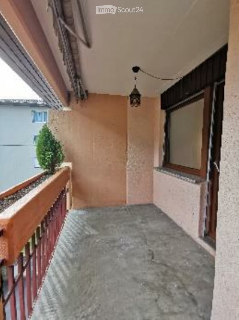 Balcony with wooden railing, small potted plant, window, and hanging light fixture.