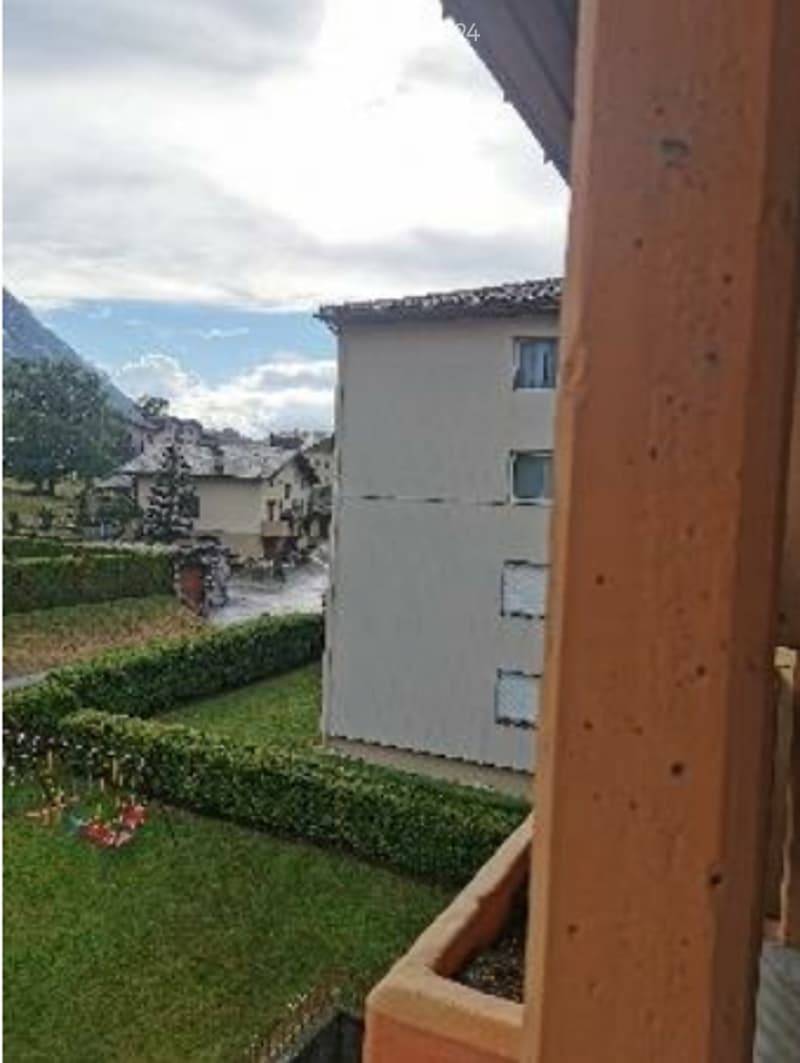 Balcony overlooking a landscaped garden with a view of mountains and neighboring buildings.