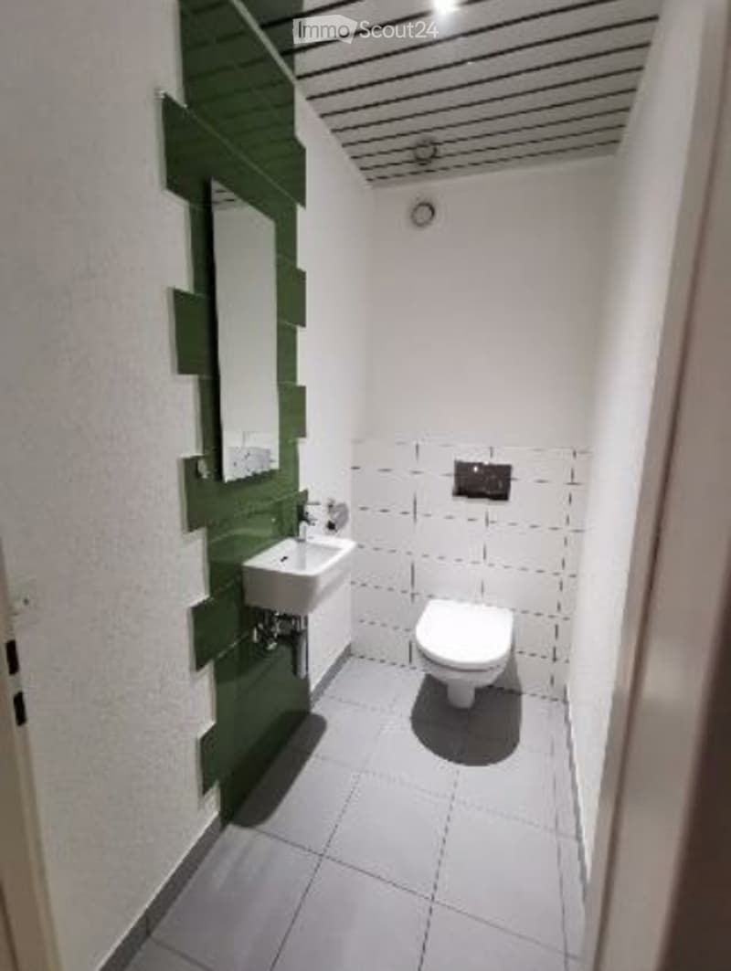 Modern bathroom with white tiles, green accent wall, sink, toilet, and mirror.