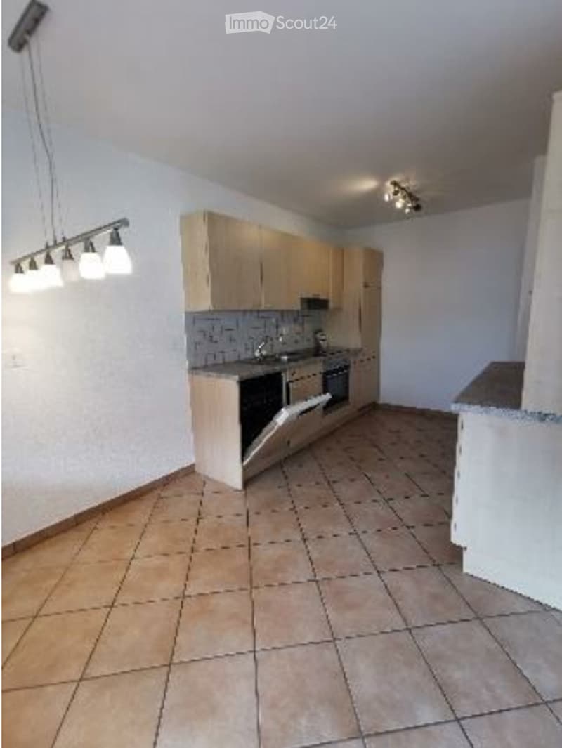 Modern kitchen with light wood cabinets, stainless steel appliances, and tiled flooring.