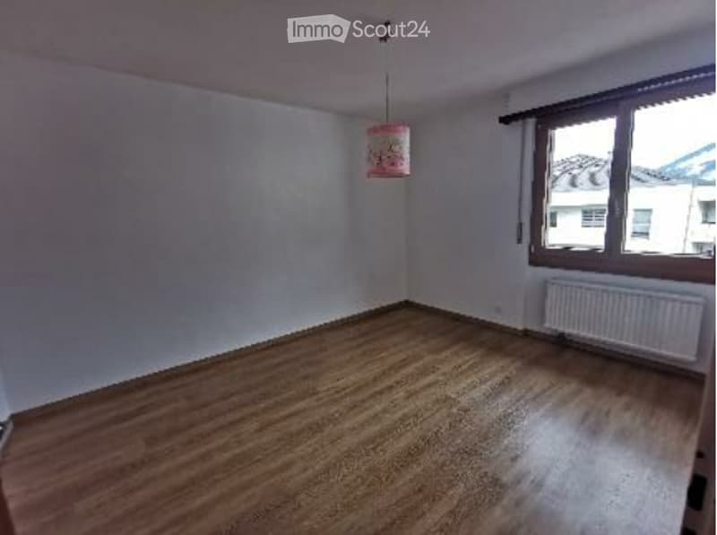 Empty room with wooden flooring, white walls, a window with wooden frame, and a radiator under the window. No furniture or equipment present.