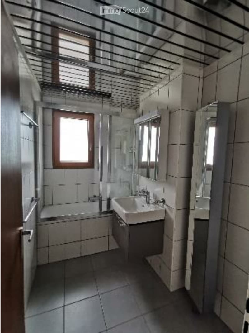 Modern bathroom with white tiles, a sink, a bathtub, and a mirror. The space features a window with blinds and a sleek, contemporary design.