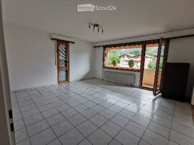 Empty room with white walls, tiled floor, large window with wooden frame, and a door with glass panel.