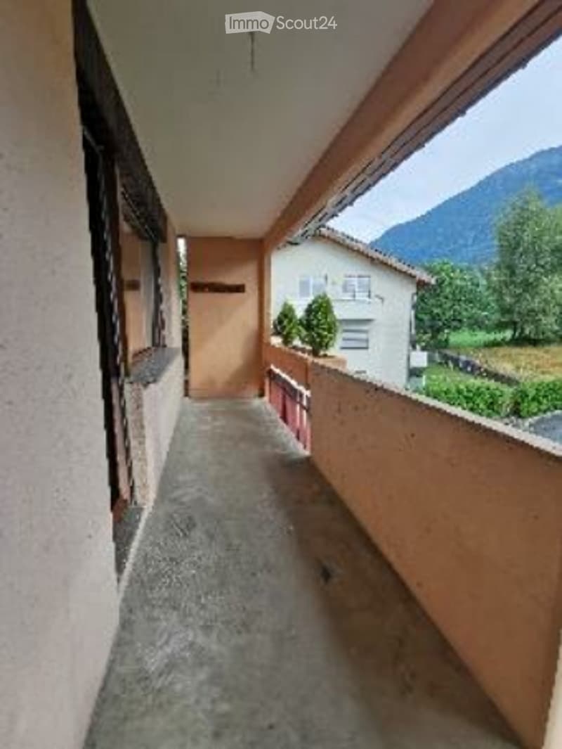 Balcony with a view of mountains and neighboring houses, concrete floor, simple railing, small potted plants.