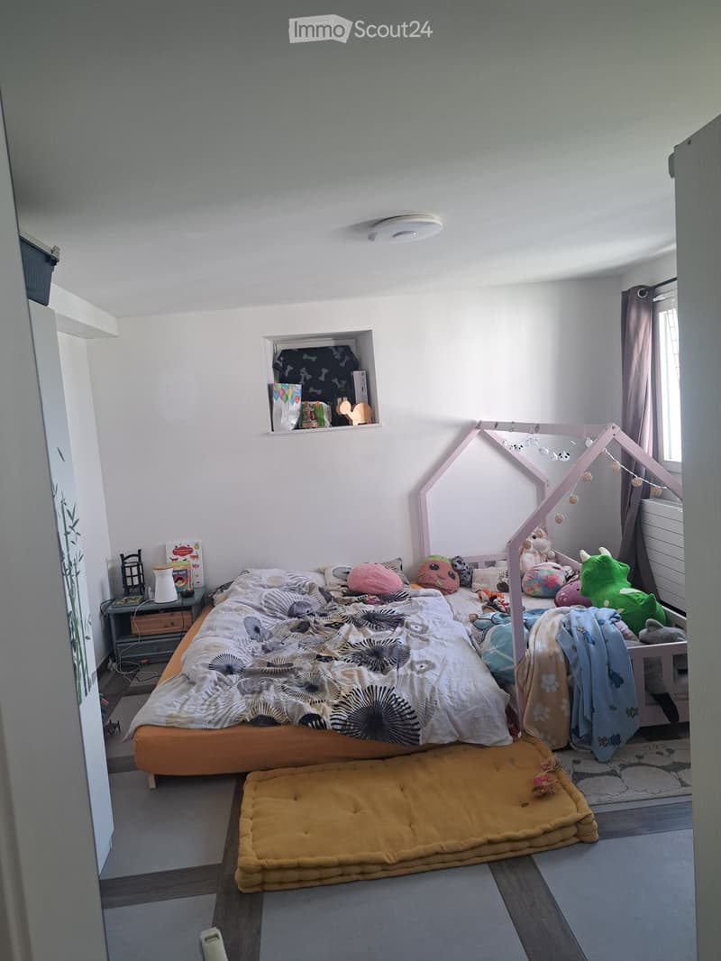 A cozy children's bedroom with a bed, colorful pillows, a blanket, a small tent for play, stuffed animals, a dog bed, a nightstand, and a shelf with books and toys.