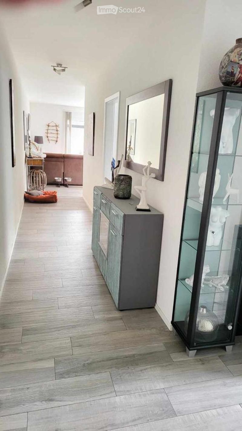 Modern hallway with light wood flooring, white walls, and contemporary decor including a sideboard, glass cabinet, and artwork.