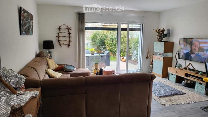 Modern living room with large sliding glass doors leading to a patio, a brown sectional sofa, a coffee table, a television, and decorative items including a floor lamp and side table.