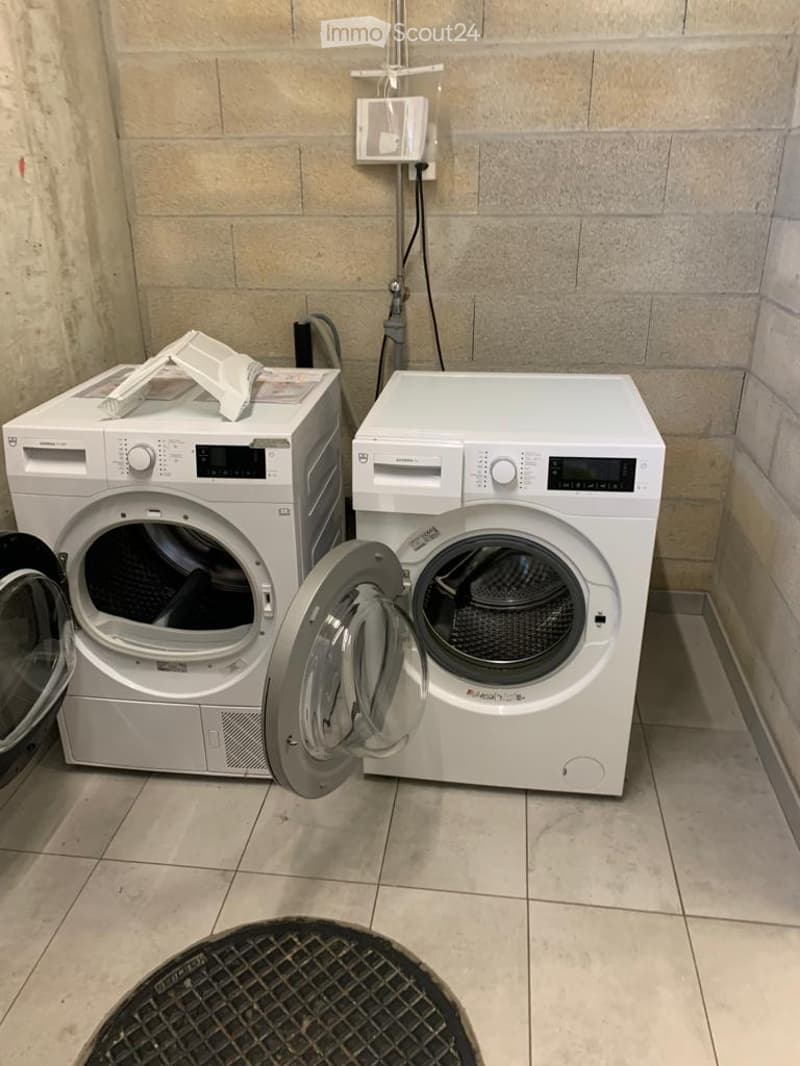 A small bathroom with a washing machine and dryer, both white, placed side by side against a tiled wall.