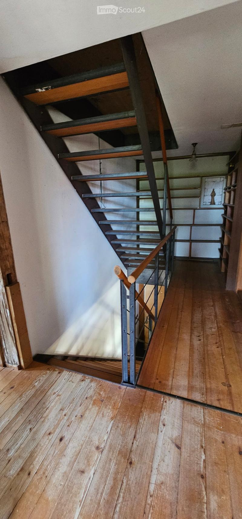 Wooden staircase with metal railing, wooden floors, and exposed wooden beams on the ceiling.