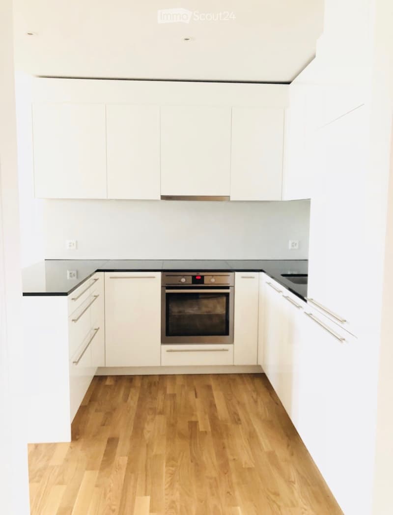 Modern kitchen with white cabinets, wooden flooring, and a built-in oven.