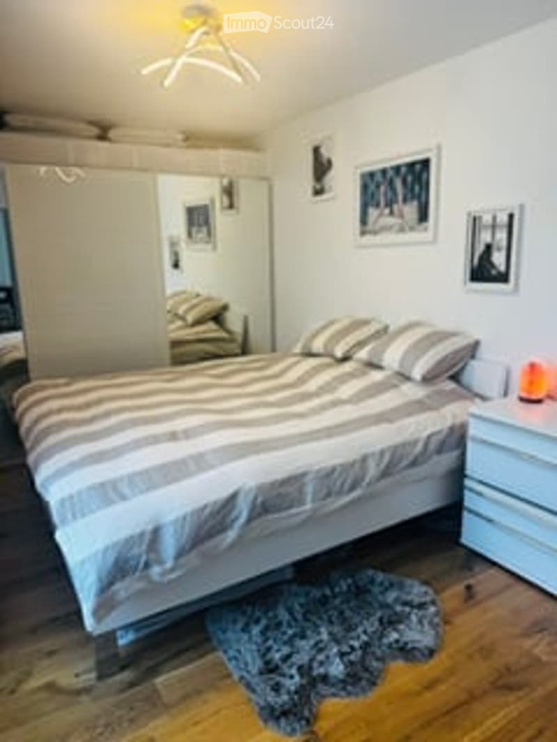 Cozy bedroom with a neatly made bed, nightstand, mirror, and decorative picture frames on the wall.