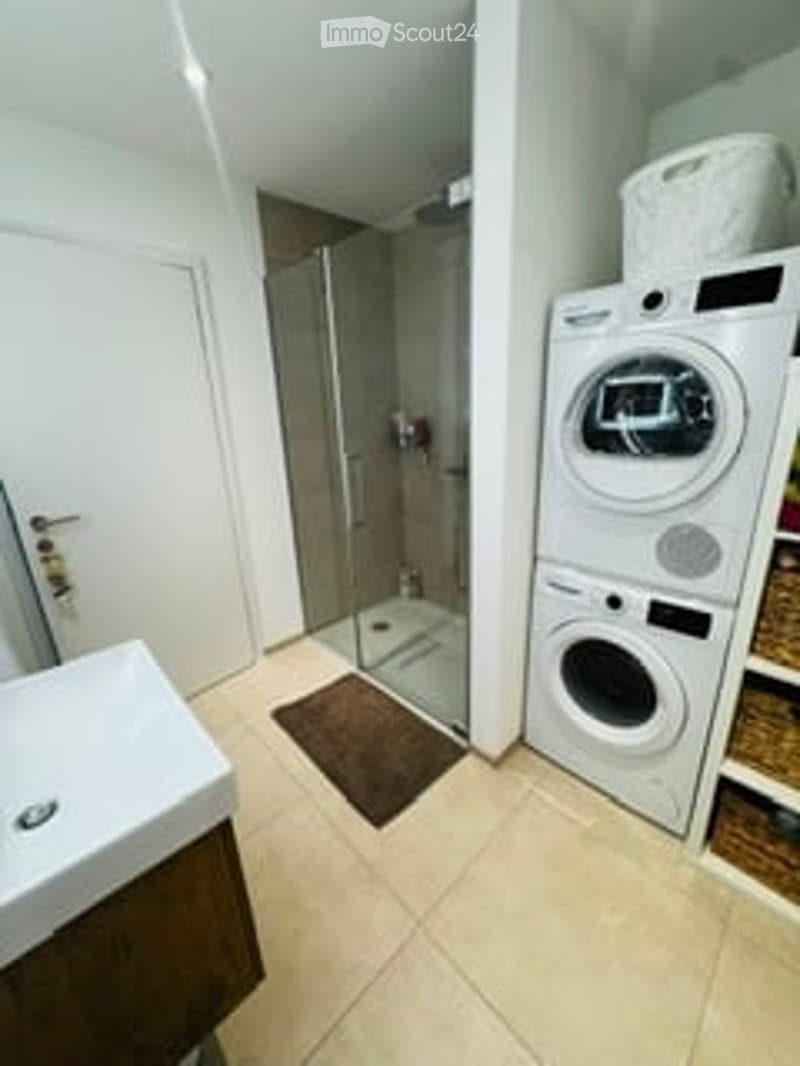 Modern bathroom with a white sink, tiled floor, glass shower enclosure, and a private washing machine and dryer unit.