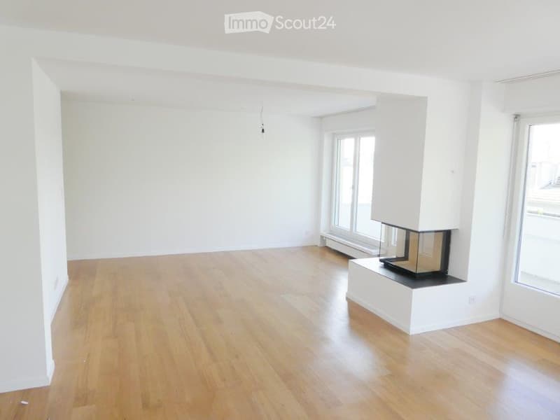 Empty room with light wooden flooring, white walls, and a built-in fireplace with a glass front.