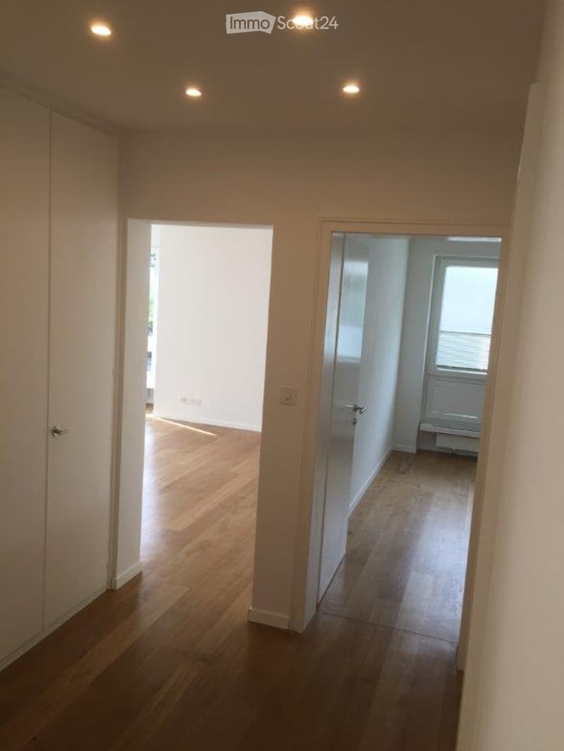 Empty hallway with wooden flooring, white walls, and recessed lighting. Two open doorways lead to adjacent rooms.