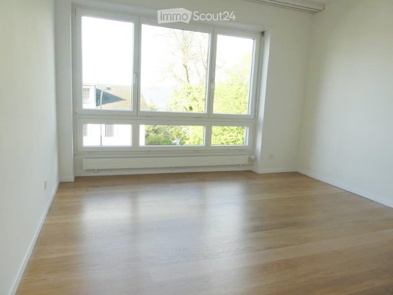 Empty room with wooden flooring, large windows, and white walls.