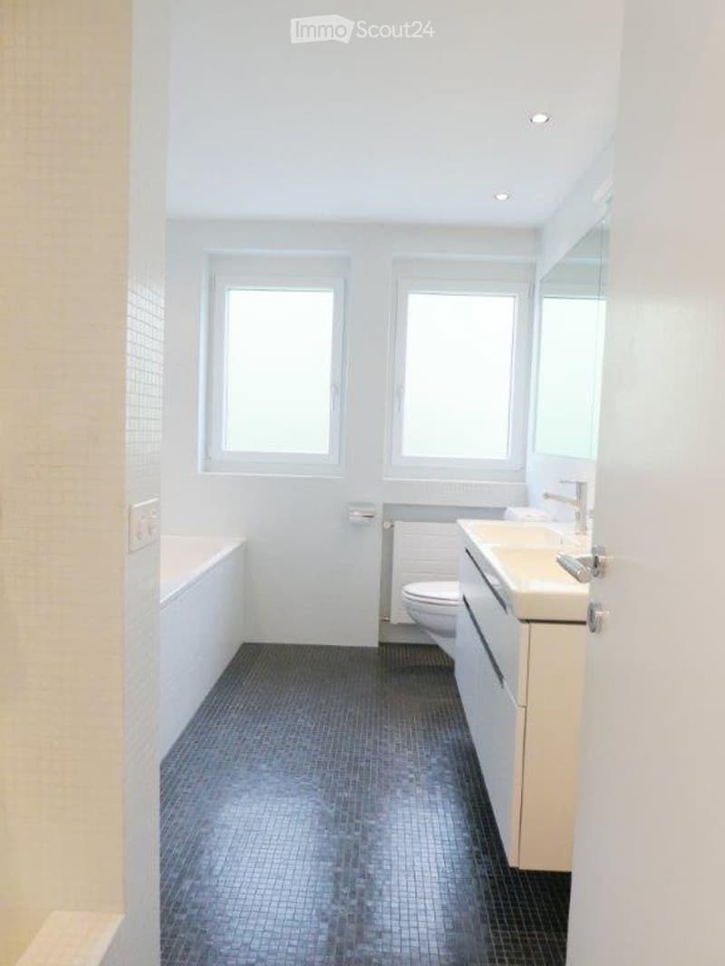 Modern bathroom with white walls, dark grey tiled floor, bathtub, toilet, sink, and mirror.