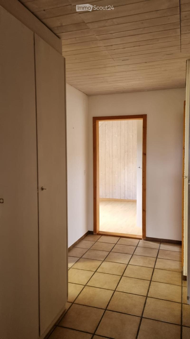 Empty room with tiled floor, wooden ceiling, white walls, wooden door, and a door leading to another room