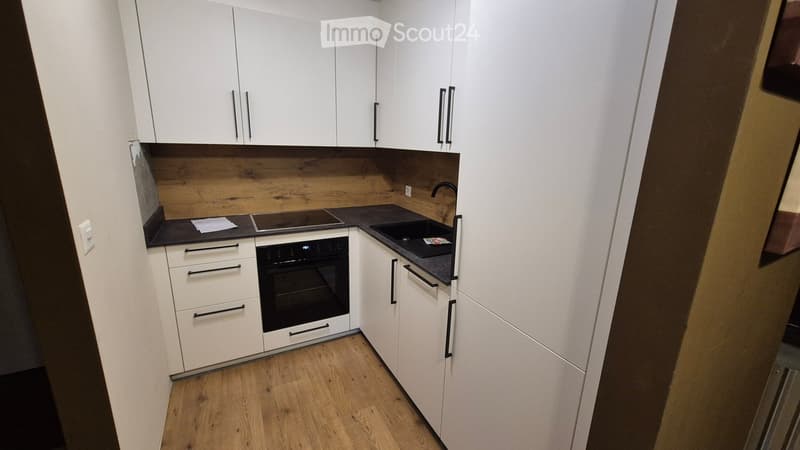 Modern kitchen with white cabinets, wooden accents, and a black countertop. Features an oven, sink, and faucet.