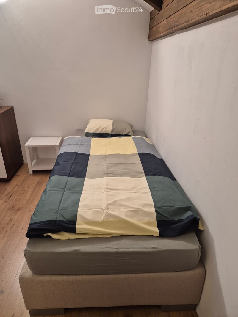 Cozy bedroom with a single bed, grey and blue bedding, a nightstand, and a wardrobe.