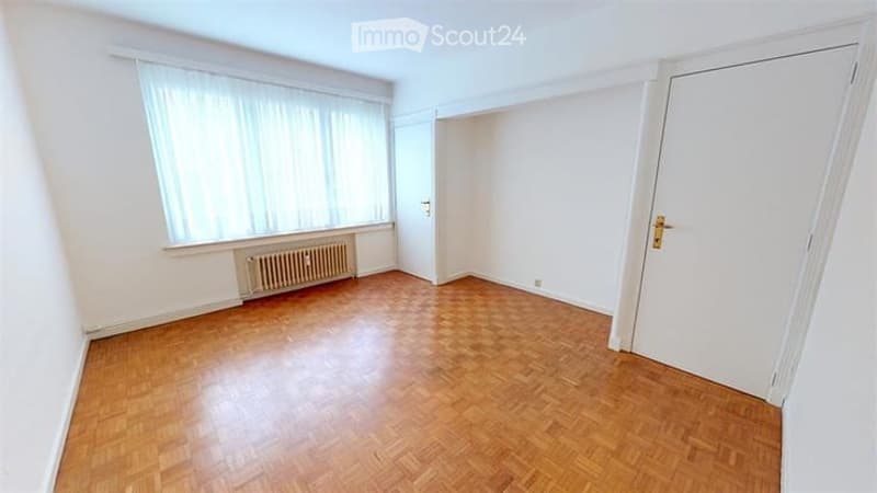Empty room with wooden flooring, white walls, large window with blinds, radiator, and white door.