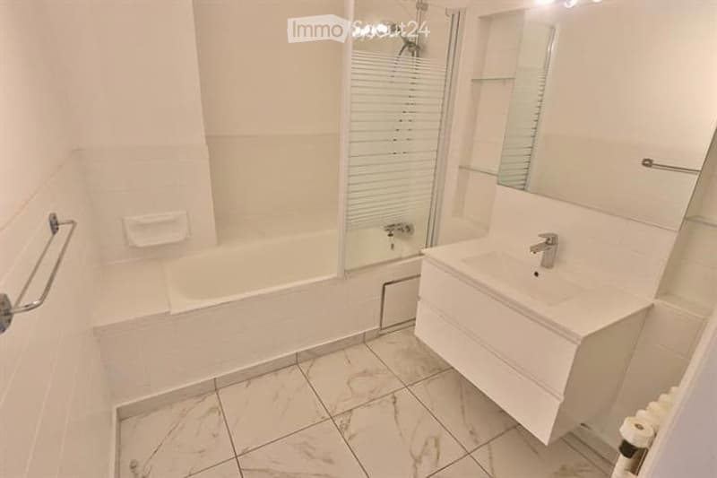 Modern bathroom with a white bathtub, a white sink with a modern faucet, a large mirror, a glass-enclosed shower, and a white tiled floor.