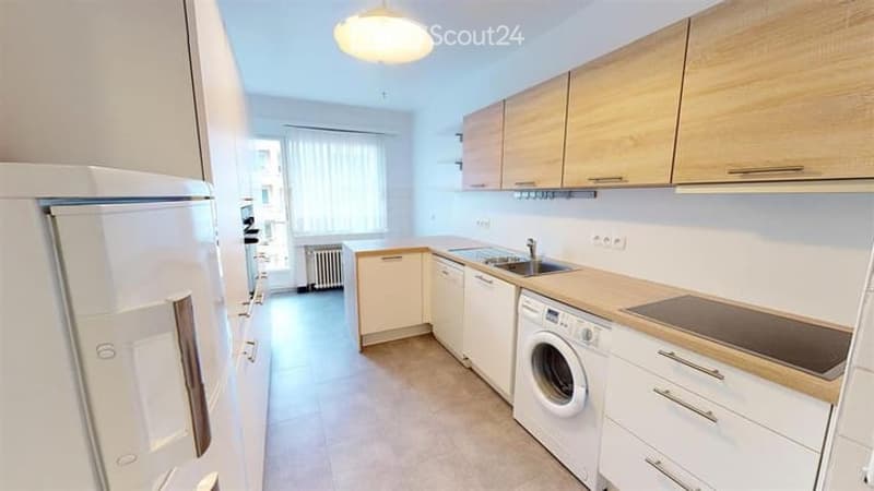 Modern kitchen with white cabinets, light wood countertops, stainless steel appliances including a refrigerator, dishwasher, and washing machine, and a central island with a sink.