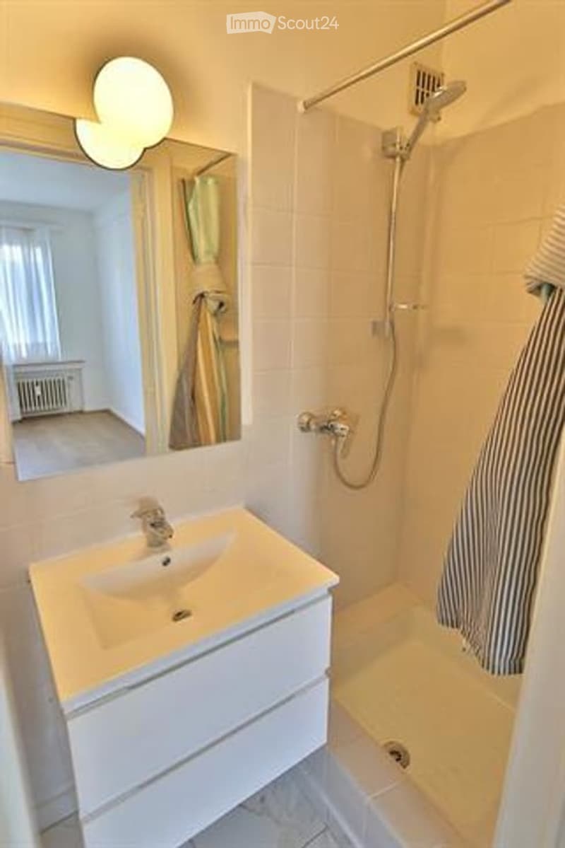 Modern bathroom with a white sink, mirror, shower, and towel visible.