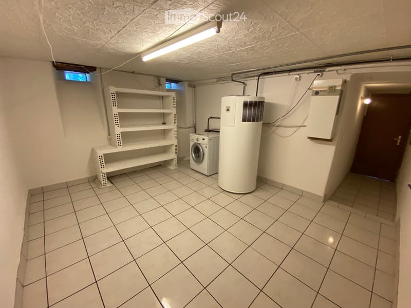 Utility room with tiled floor, white walls, washing machine, water heater, and shelving unit.
