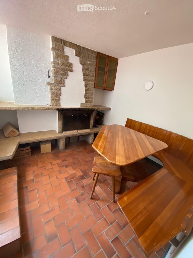 Room with a stone fireplace, wooden table, chairs, and a bench, featuring a tiled floor and wooden cabinet.