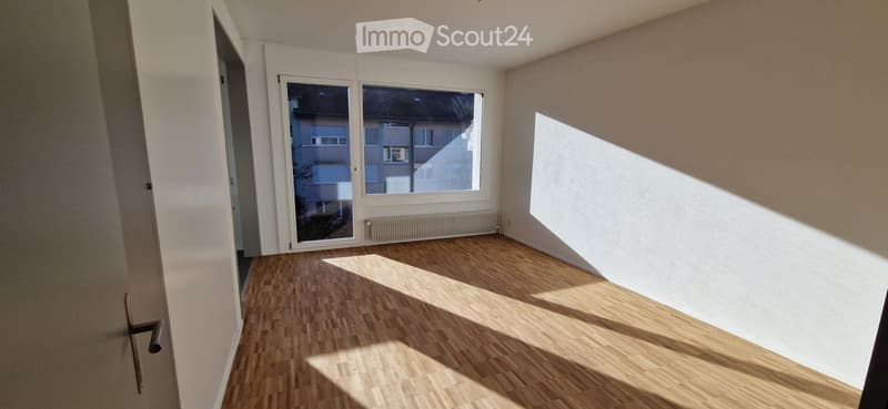 Empty room with wooden flooring, white walls, large windows, and a radiator. No furniture or equipment present.