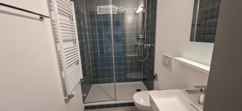 Modern bathroom with a glass-enclosed shower, white towel rack, toilet, sink, and a sleek window with blinds.
