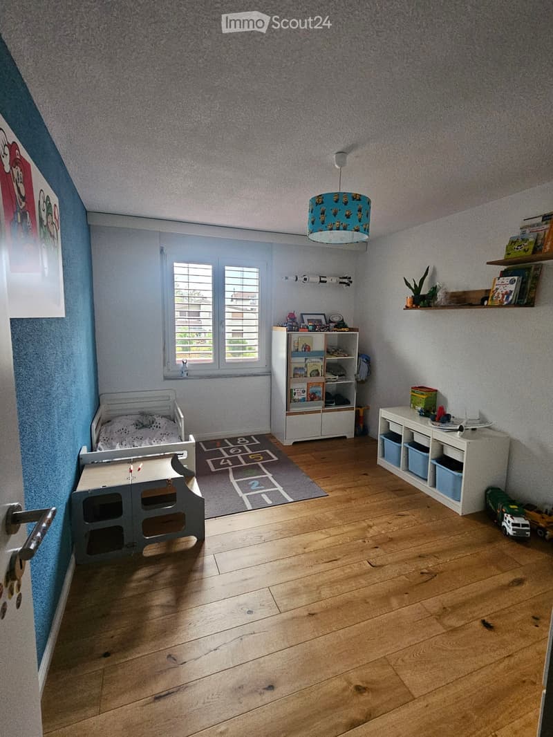 Child's bedroom with wooden floor, bed, bookshelf, small table, and toys.