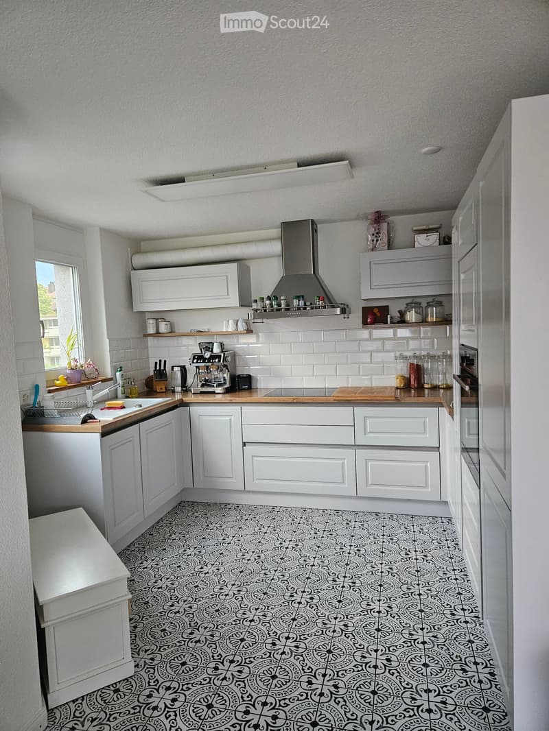 Modern kitchen with white cabinets, stainless steel appliances, and a patterned black and white tile floor. Features a coffee maker, sink, and various jars on the counter.