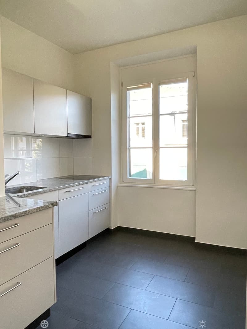 Modern kitchen with white cabinets, granite countertop, and a double sink. The room features large windows and dark tiled flooring.