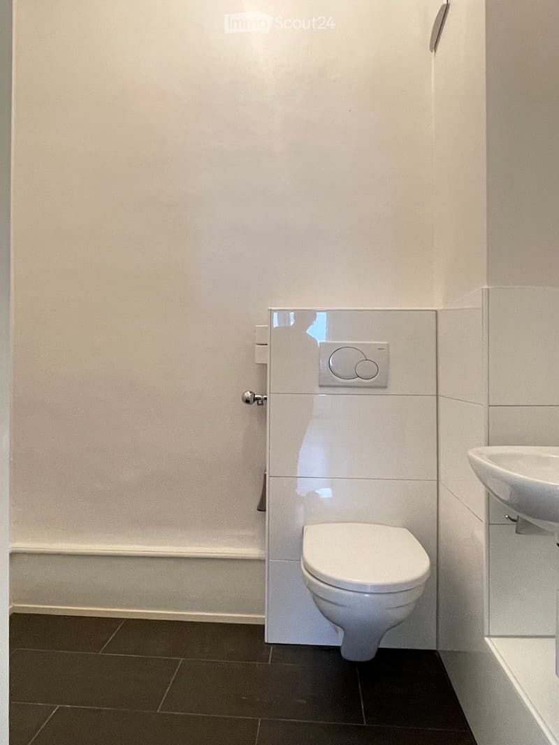 Modern bathroom with a toilet, sink, and sleek white tiles on walls and floor.